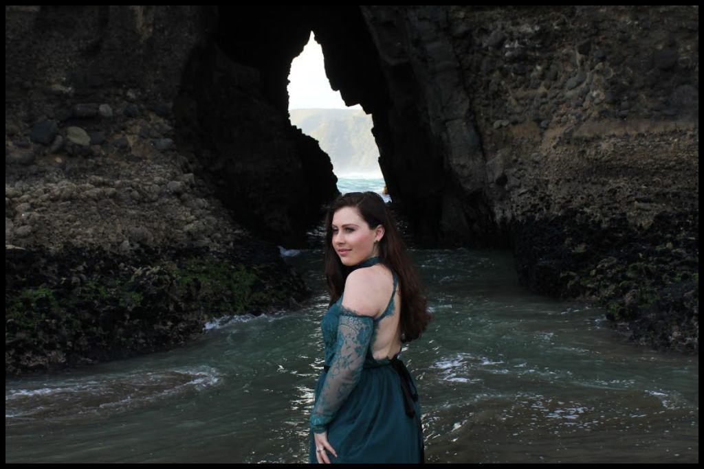 Young woman (author) stands ankle deep in the currents with The Keyhole behind her.