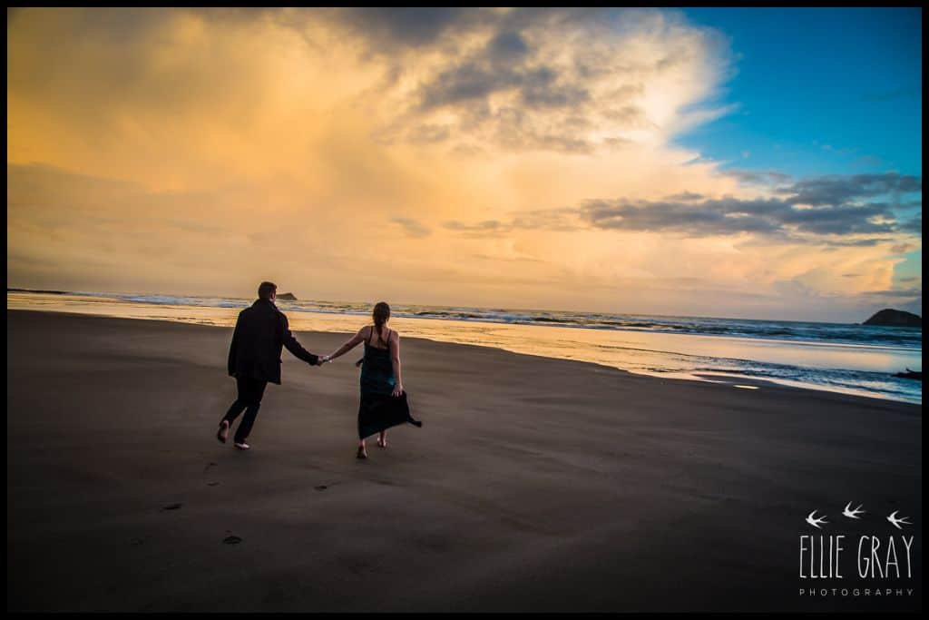 Silhouetted couple run toward the waves at sunset, at Maori Bay.