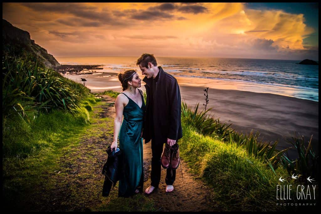 Young couple gaze at each other with the sun setting at Māori Bay in the background.