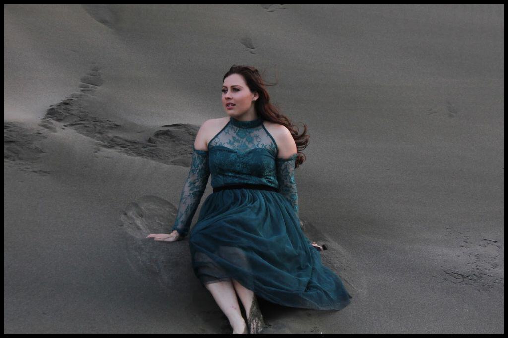 Young woman (author) sits in the black sand dunes at Piha Beach.