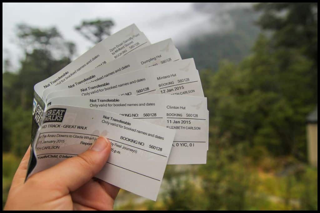 A hand holds out Milford Track bookings, splayed out.