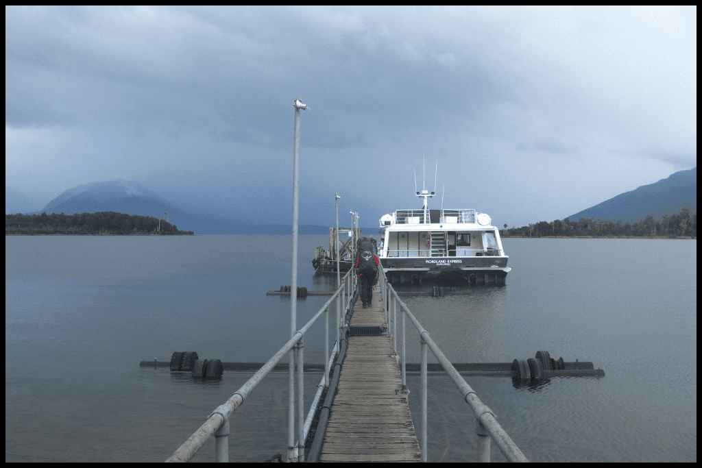 Figure with hiking pack retreats down the jetty toward the boat at Te Anau Downs.