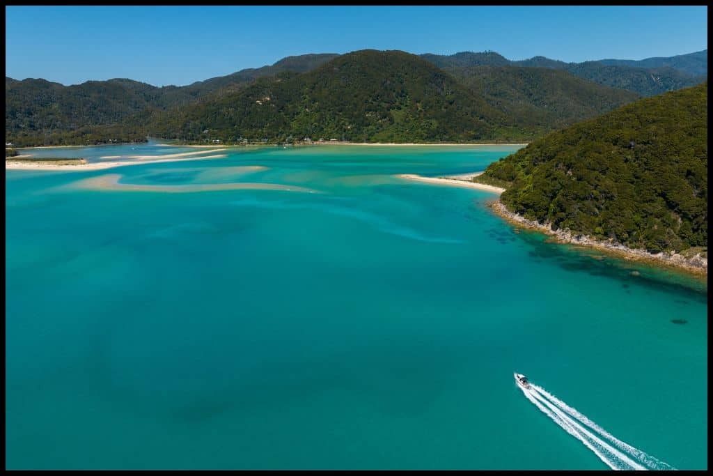 Aerial shot shows the turquoise waters of the Abel Tasman Coast and an Abel Tasman Aqua Taxi jetting across the water.