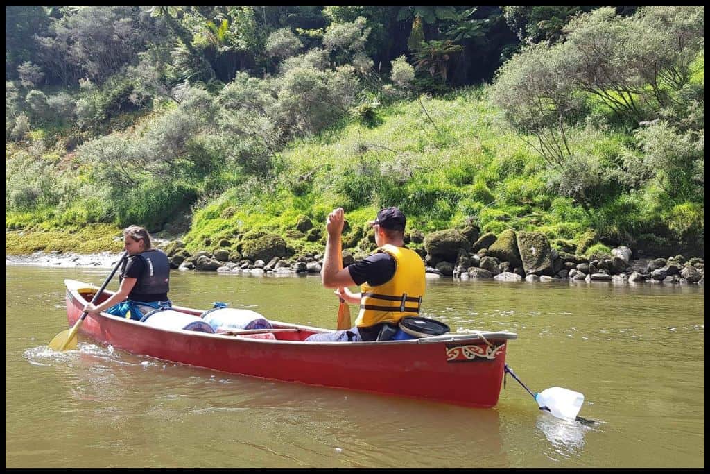 Couple paddle a two person canoe away from the camera and down the Whanganui River.