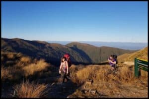 Two young women with their hiking packs on traverse the Moonlight Tops on their way to the Moonlight Tops Hut on the Paparoa Track.