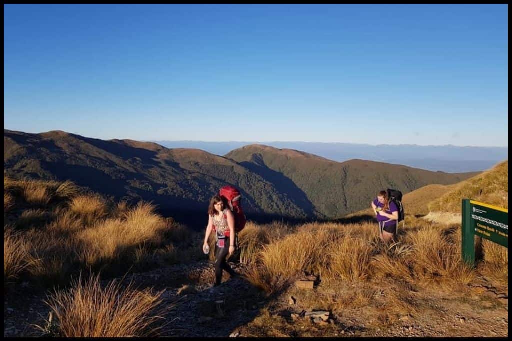Two young women with their hiking packs on traverse the Moonlight Tops on their way to the Moonlight Tops Hut on the Paparoa Track.