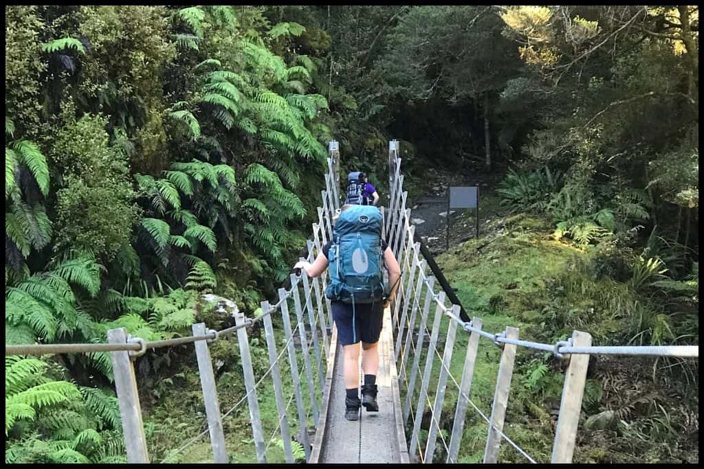 Photo shows a hiker retreating over the first swingbridge on the Paparoa Track, going northbound.