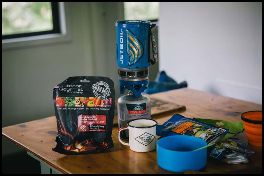 The photo shows a dehydrated tramping meal, mug, gas cooker and dinnerware on one of the tables at the huts.