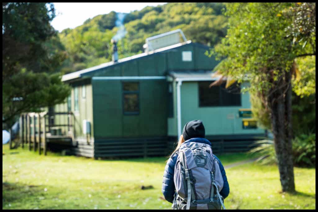 Photo captures the back of a hiker approaching the Department of Conservation hut on the Rakiura Track.