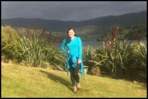 A young woman (the author) poses in her hiking gear in front of the North Arm Hut with a dark stormy sky behind her.