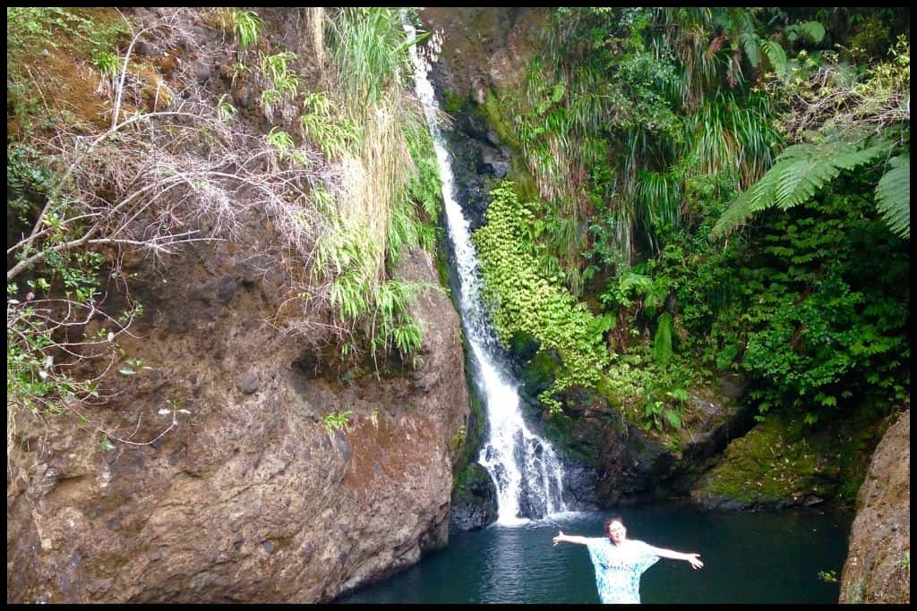 Young woman poses with arms spread wide in front of Karamatura Falls.