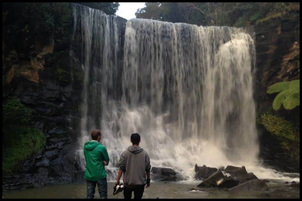 Two males face away from the camera looking up at Mokoroa Falls.