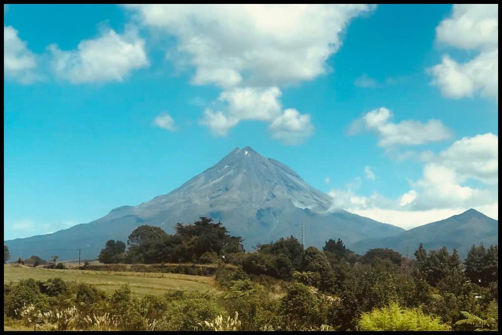 The bald cone of Mount Tāranaki dominates the horizon under a mid-summer sky.