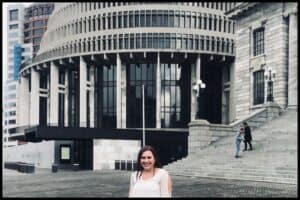 Young woman stands in the foreground with the Beehive, New Zealand's. parliamentary building, in the background.