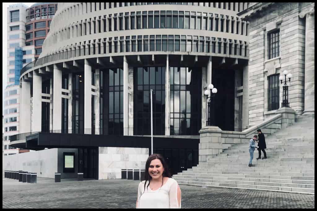Young woman stands in the foreground with the Beehive, New Zealand's. parliamentary building, in the background.