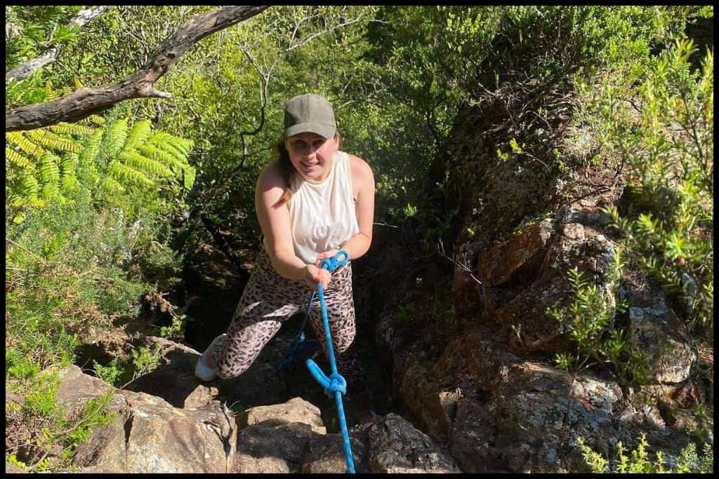 Young woman smiles up at the camera as she abseils off a rock.
