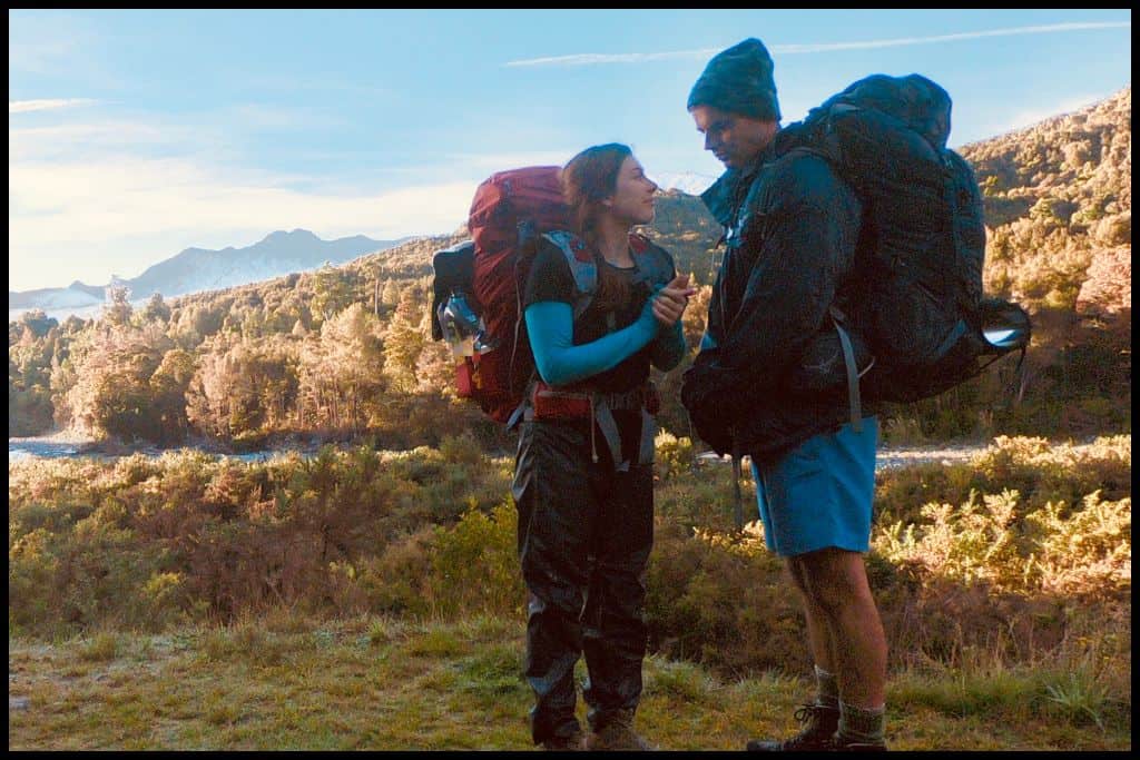 Young couple in hiking gear stand ready for the day in front of the Brown River valley, aglow with autumn colours lit up with morning sunlight.