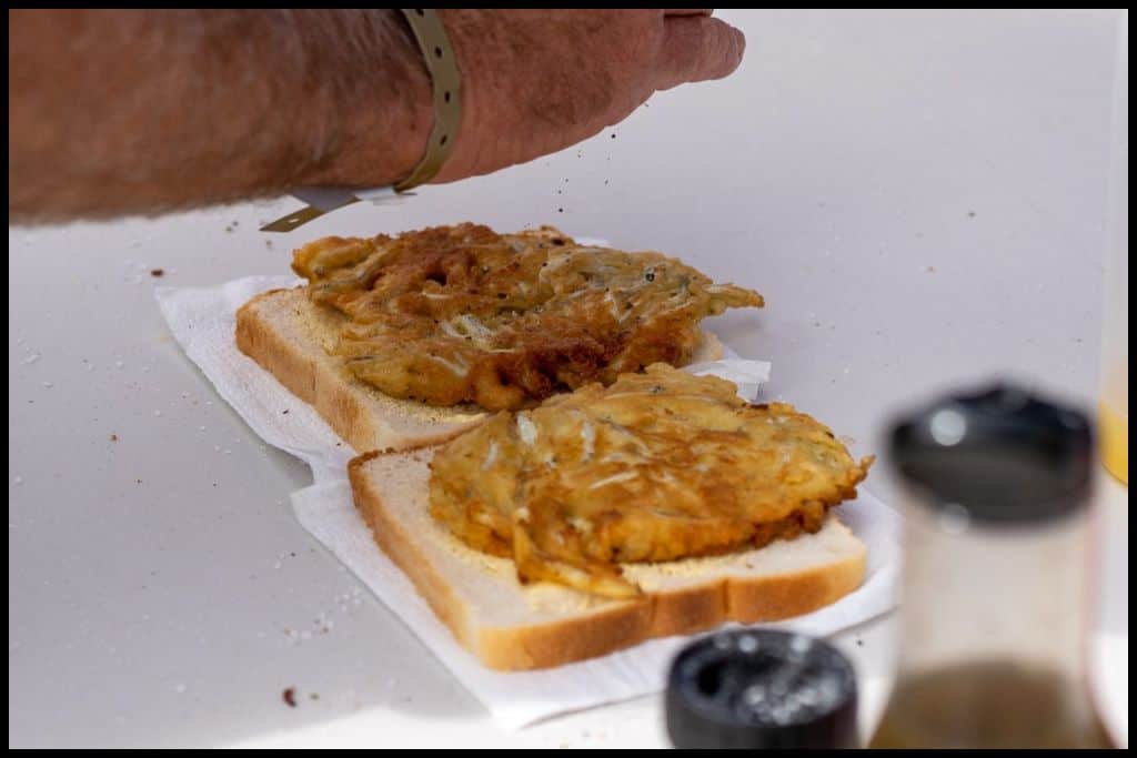A close up shot shows two whitebait fritters being prepared on white bread at the Hokitika Wildfoods Festival.