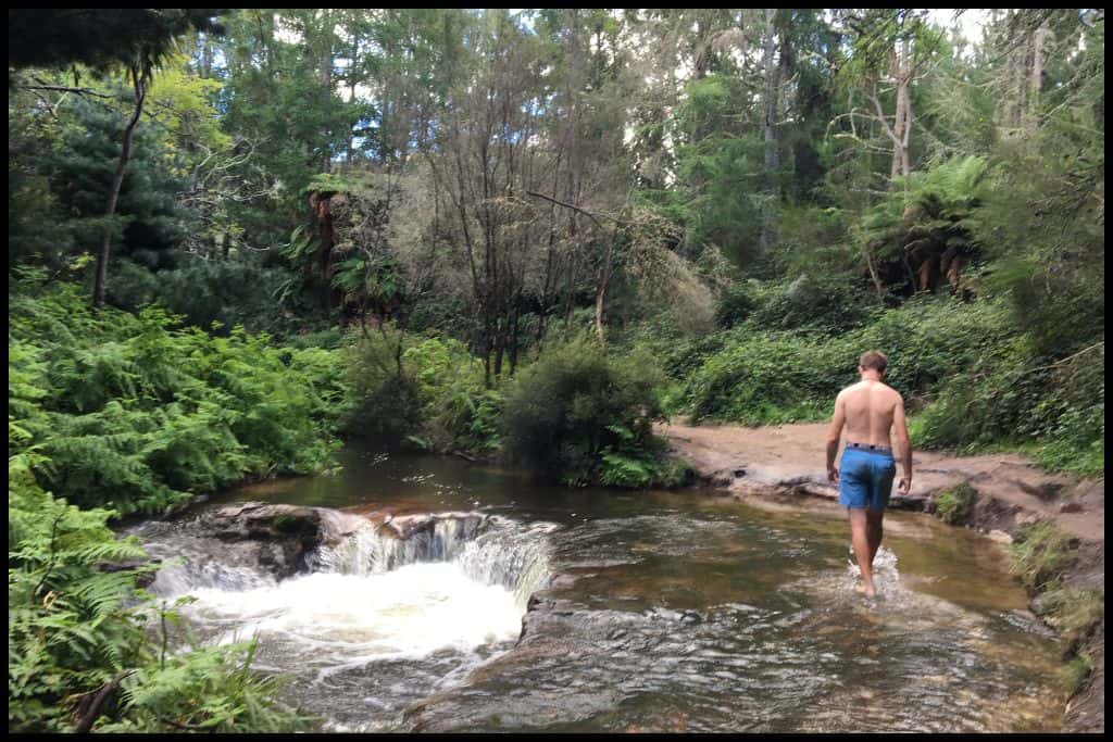 A young male walks away from the camera through ankle deep water at Kerosene Creek.