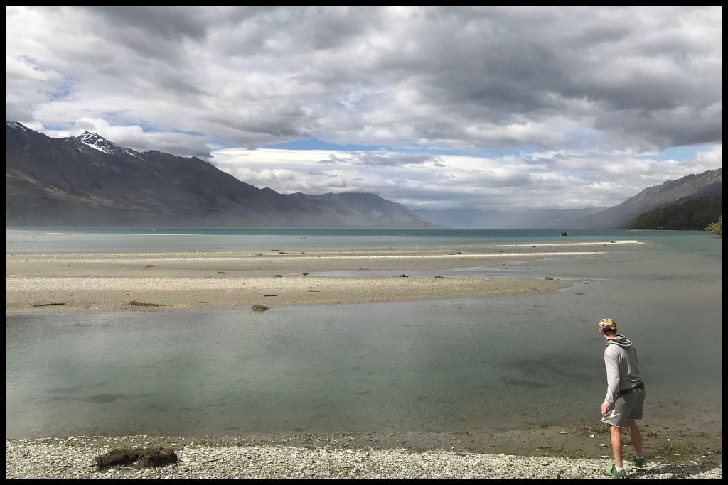 A young male skips a stone over the shallow water at the edge of Lake Wakatipu, up at Kinloch.