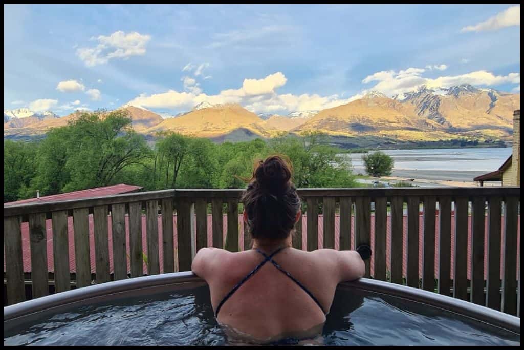 A young woman leans over the edge of a hot tub at Kinloch Wilderness Retreat and looks out over the lake.