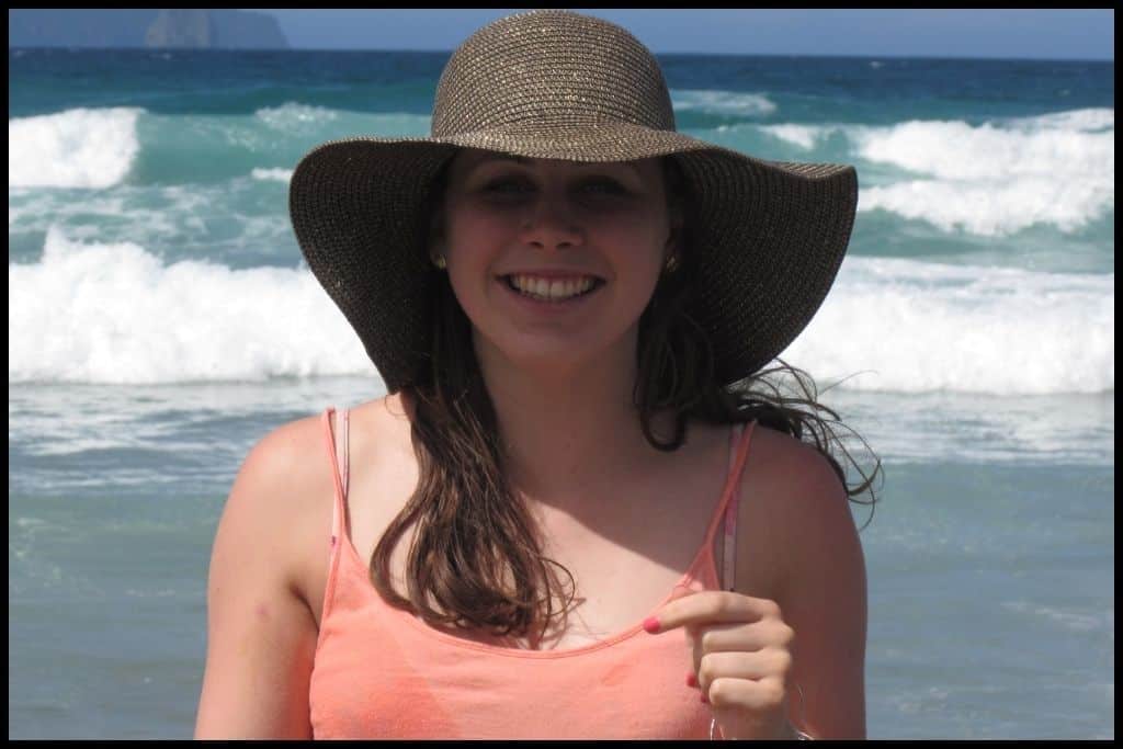 Teen girl smiles for the camera with the surf crashing behind her.