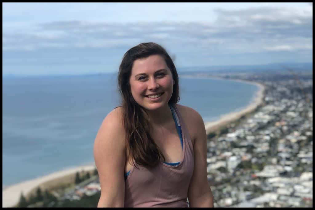 A young woman poses in front of the views from the summit of Mount Maunganui.