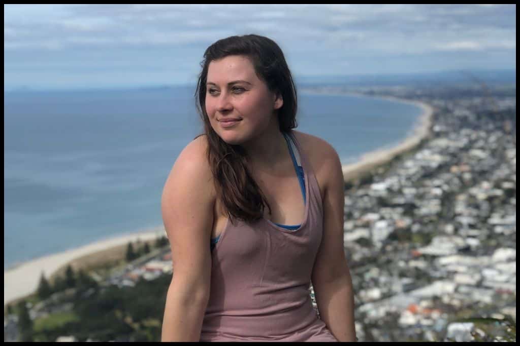 Young woman poses in front of the view from the top of Mount Maunganui.