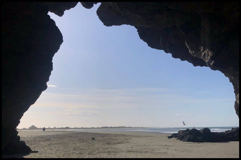 Photo looks out through the silhouetted entrance to Cave Rock at Sumner Beach.