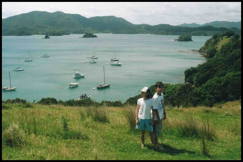 Two children stand back to back on the grassy hilltop of Urupukapuka Island in the Bay of Islands.