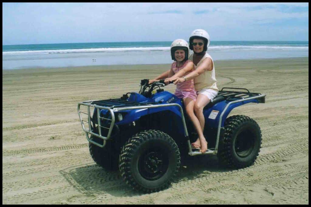 Mother and daughter sit astride a blue quad bike on Ninety Mile Beach, an official highway.