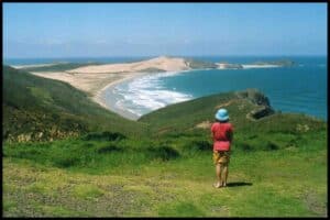 Young girl stands looking out to the sand dunes and surf at Te Werahi Beach.