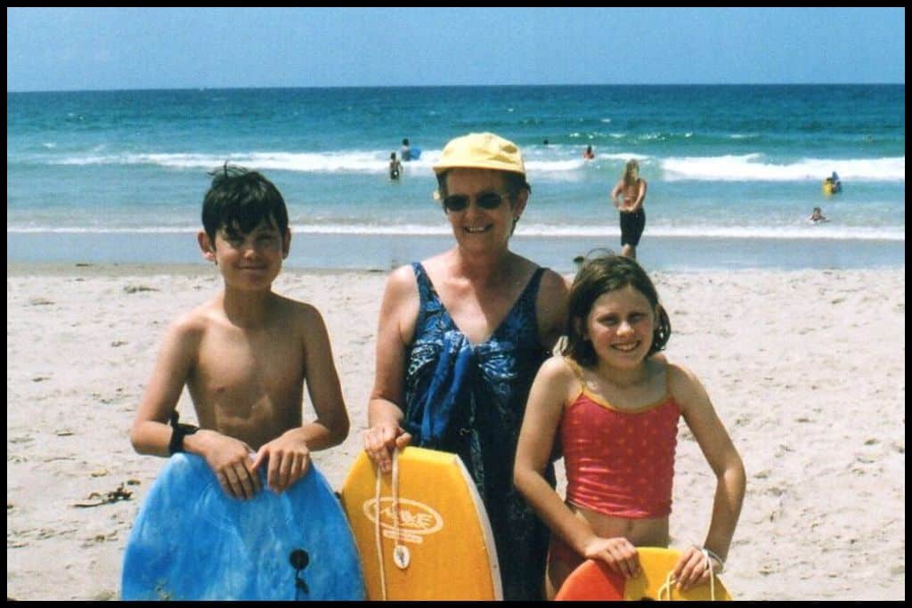 Two children and their mother smile for the camera with their boogie boards and the blue surf of Ocean Beach behind them.