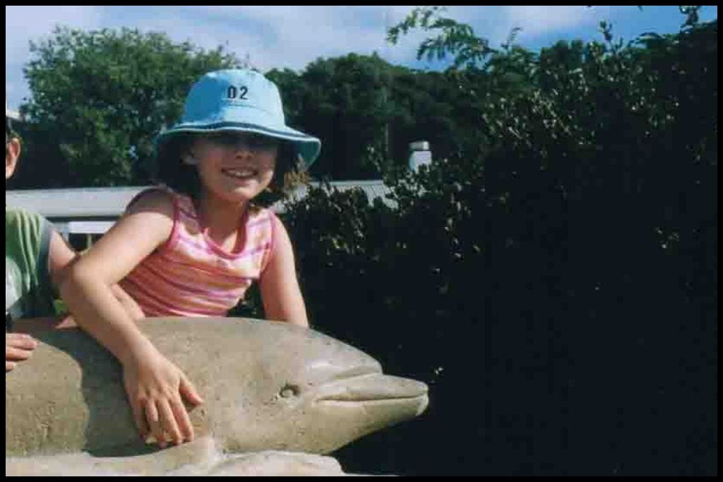 A young girl poses with the statue of Opo the Dolphin, famous at Opononi Beach in the 1950s.