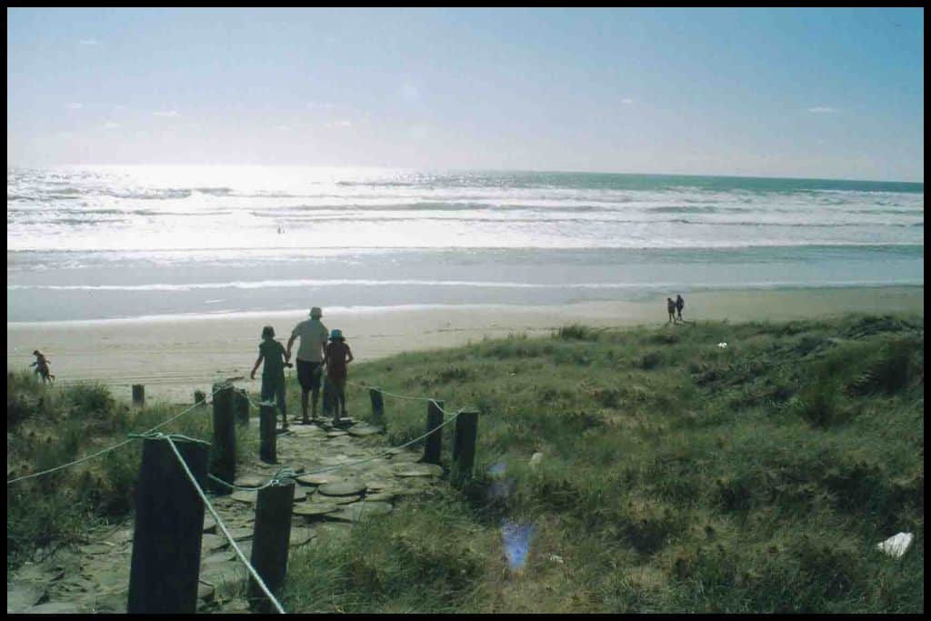 A trio of people make their way down the stone pathway to an expansive surf beach.