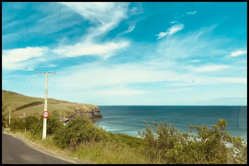 An old road weaves up onto the Otago Peninsula with cliffs and sea on the right hand side.