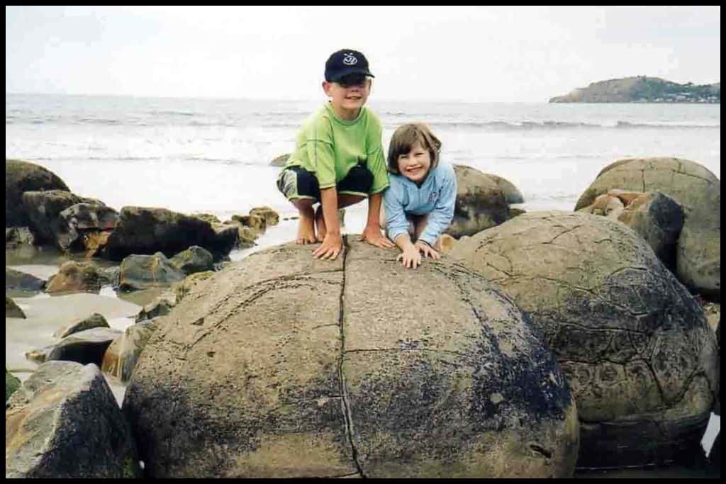 Two children smile together having clambered onto the top of one of the famous Moeraki Boulders.