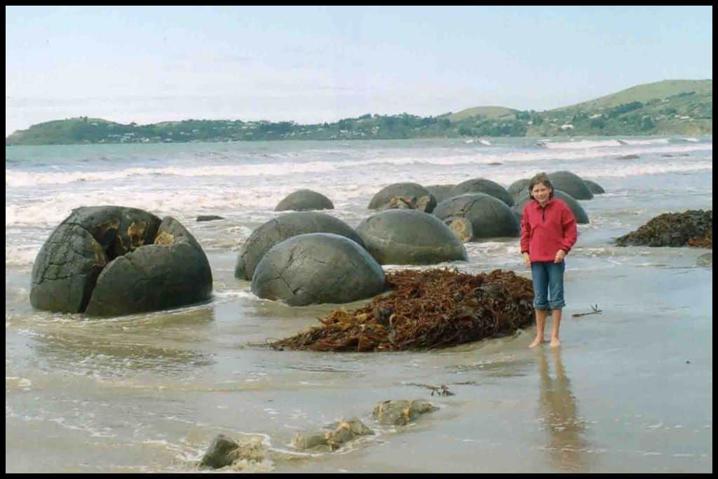 A young girl stands ankle deep in the water that swirls around the base of the infamous Moeraki Boulders.