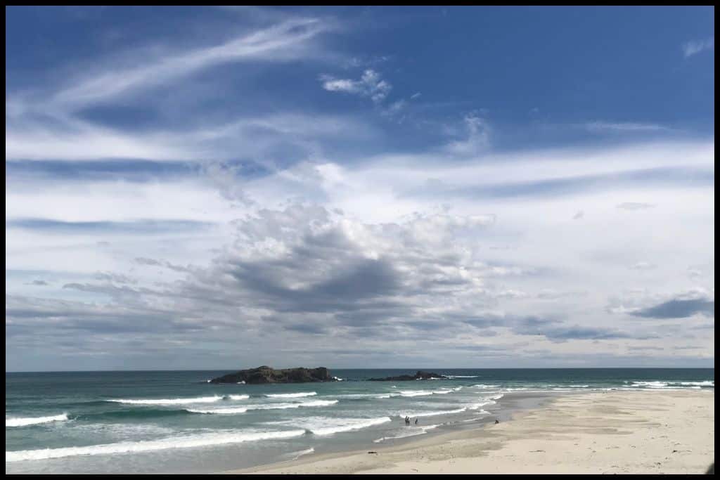 Dramatic moody clouds hover over an offshore island and the deep green sea at Smaills Beach.