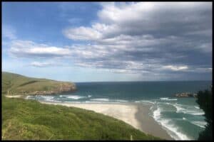 Smaills Beach, pictured from a high vantage point, with the triangle of white sand and surf crashing in two directions.