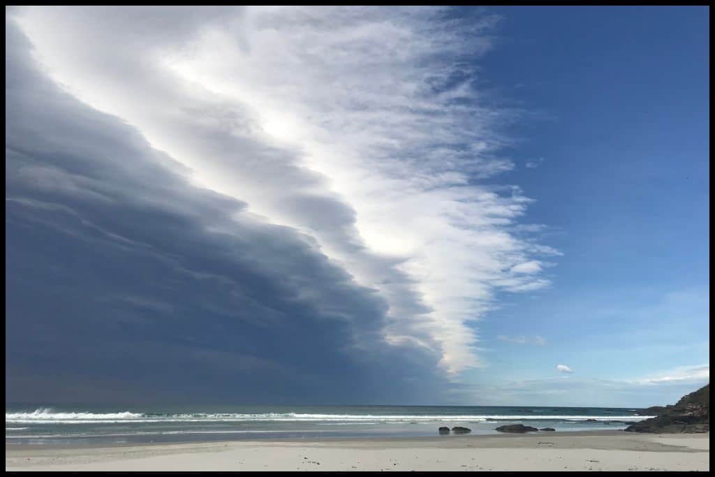 Layers of cloud that look like waves upon waves hover over the surf and sand on St Kilda Beach.