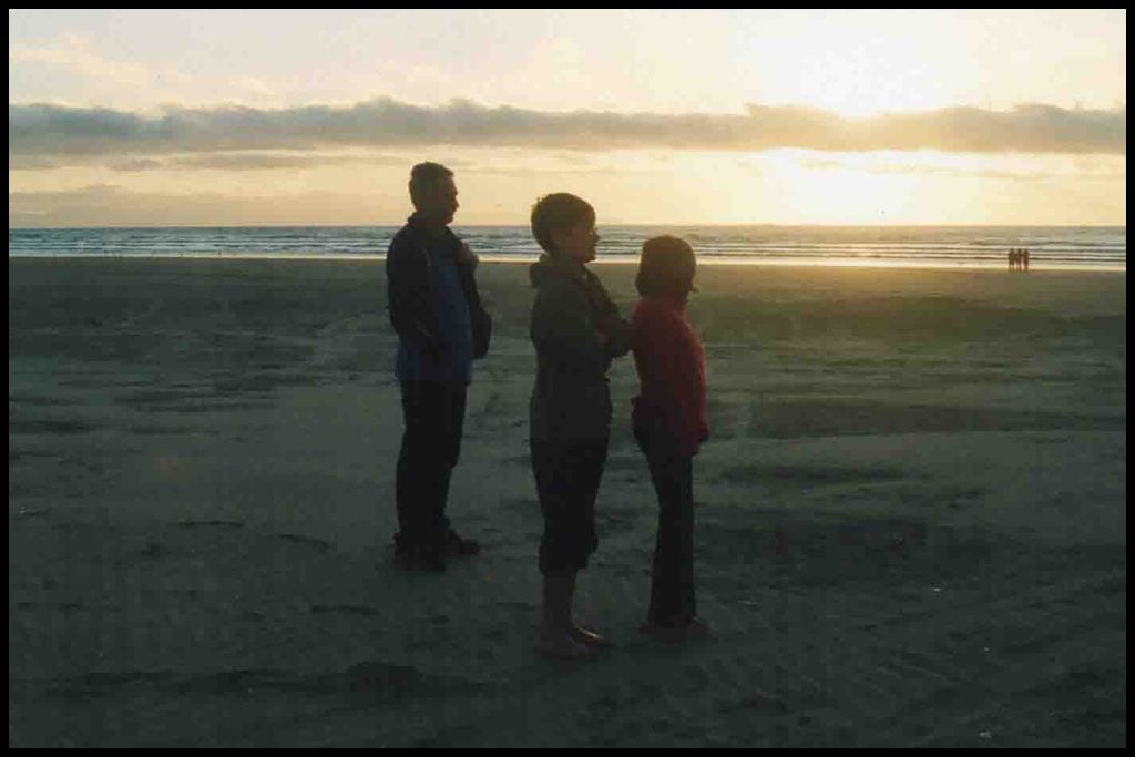 A father and his two children stand on the vast sands of Oreti Beach at sunset.