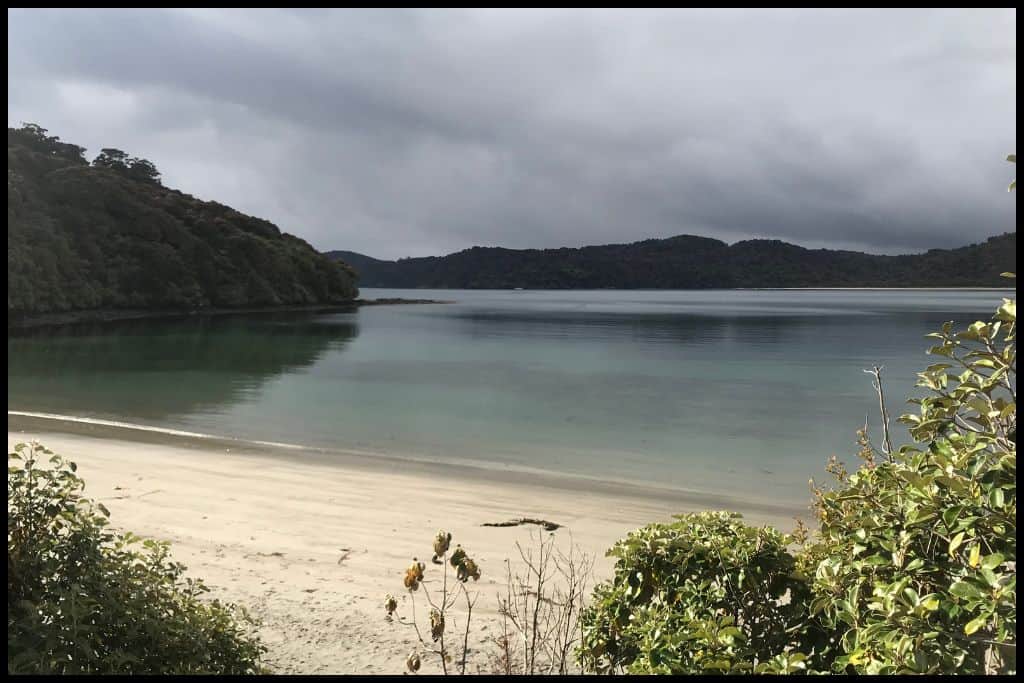 Port William Beach under a moody sky, with glassy, still sea water lapping gently onto the white sand.