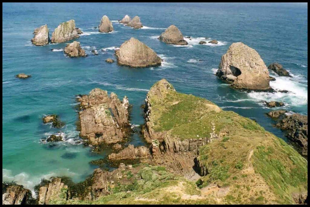 A high angle of Nugget Point shows the rock formations (nuggets) in a foaming sea green ocean.