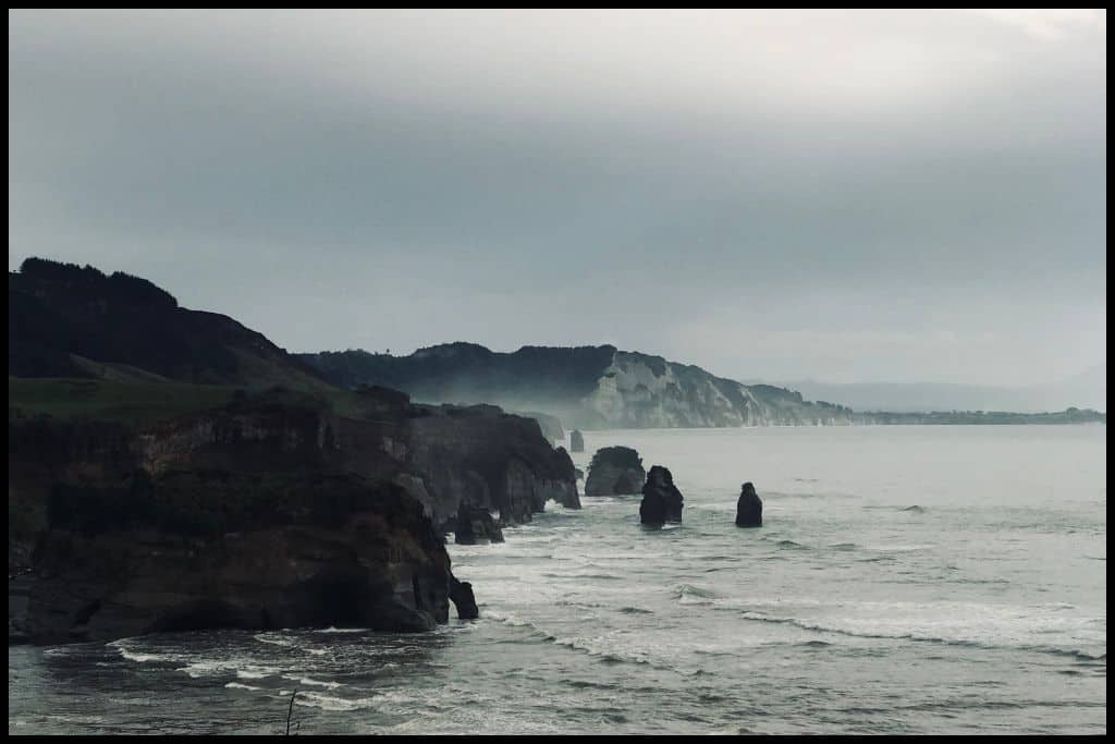 Tongaporutu Beach on a gloomy day with the Three Sisters and Elephant Rock visible in the water.