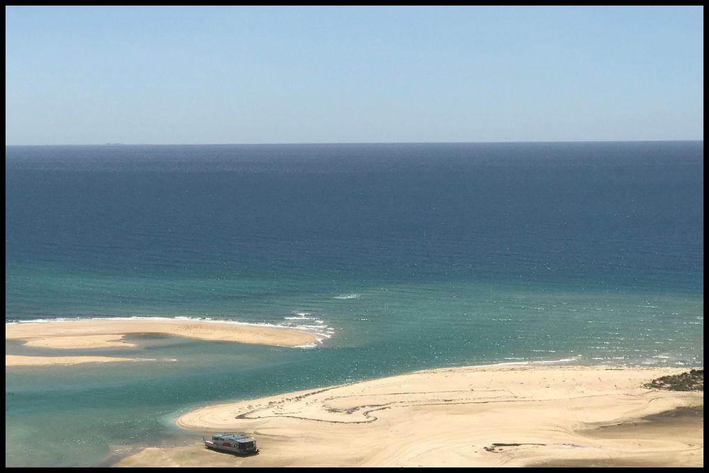 A single barge sits on the white sands below as the tide comes in to Awaroa Bay.