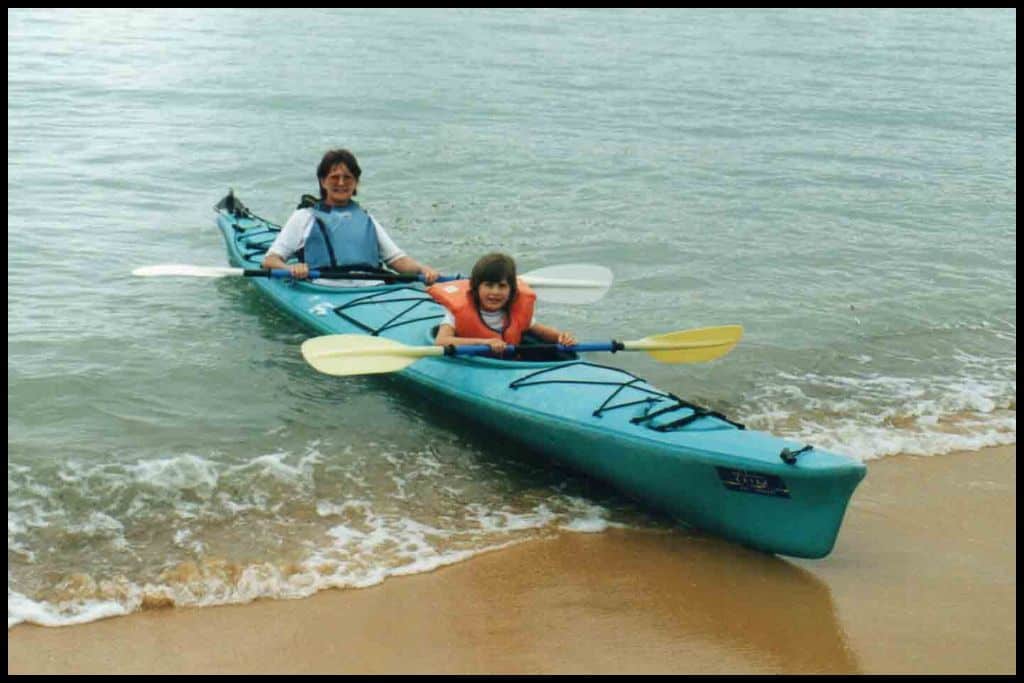 A young girl and her mother sit in a double kayak, coming ashore at Kaiteriteri Beach.