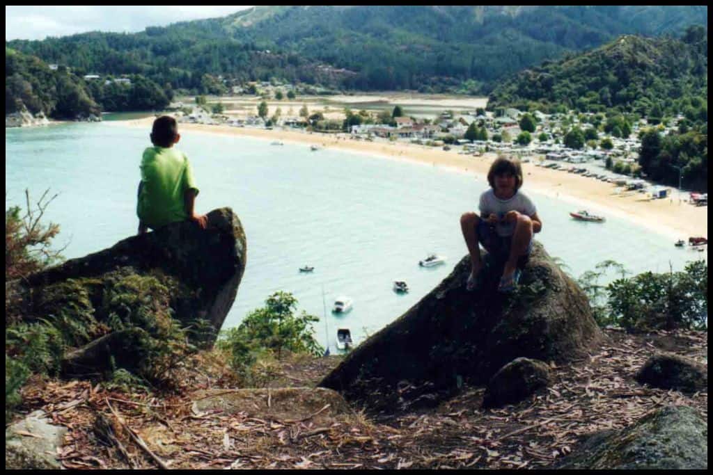 Two children sit atop rocks on a lookout high above Kaiteriteri Beach.