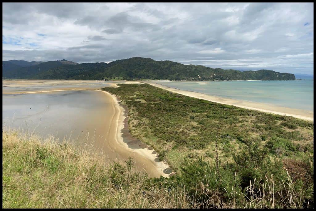 Wainui Beach and its inlet with the green foliage on the headland and sand bar pictured.