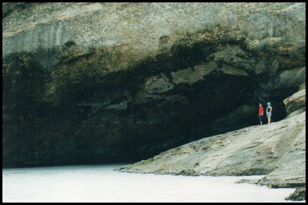 Two children stand at the mouth of a huge beach cave.